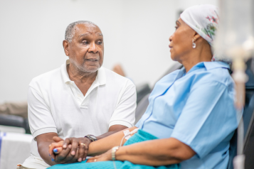 A woman in the oncology unit receiving chemotherapy treatment, accompanied by a man who is holding her hand.