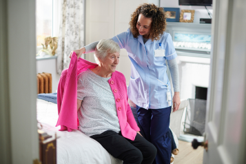 A carer helping an older woman get dressed in her home.