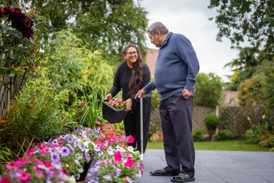 An older man using a walking stick and a younger woman gardening.